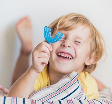 Young boy holding up blue athletic mouthguard