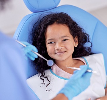 Child in blue chair smiling during dental checkup