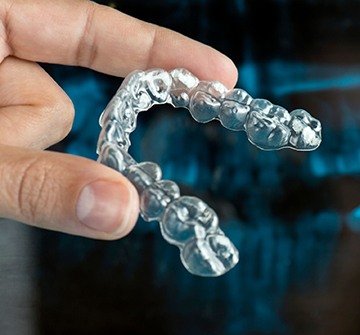 close up of a person holding Invisalign aligner in front of dental x-ray 