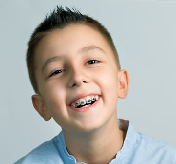A little boy smiling while wearing metal braces after seeing his orthodontist in Randolph