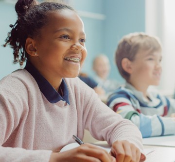 A young girl wearing a sweater and sitting in class wearing braces for Phase 1 Orthodontic treatment