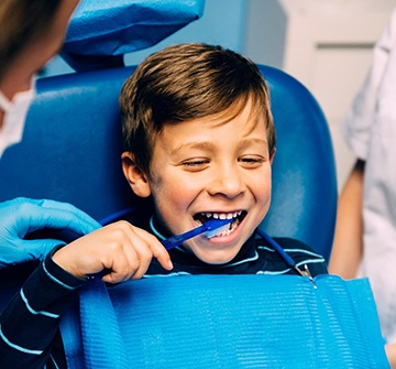 Child smiling while brushing his teeth with pediatric dentist