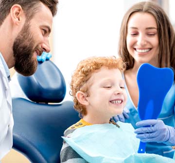 Child smiling in mirror next to sedation dentist in Randolph