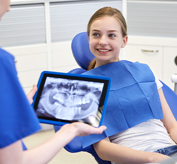Dentist looking at teen girl's digital x-rays
