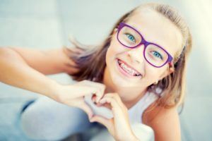 Young girl with braces making heart shape with hands after visiting Randolph orthodontist 