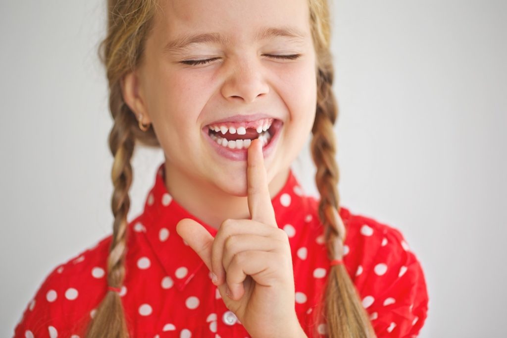 Child smiling while pointing to missing baby tooth