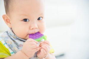 Young teething baby chewing on a teething toy