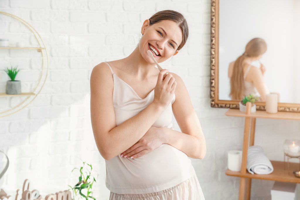Closeup of pregnant woman smiling while brushing her teeth