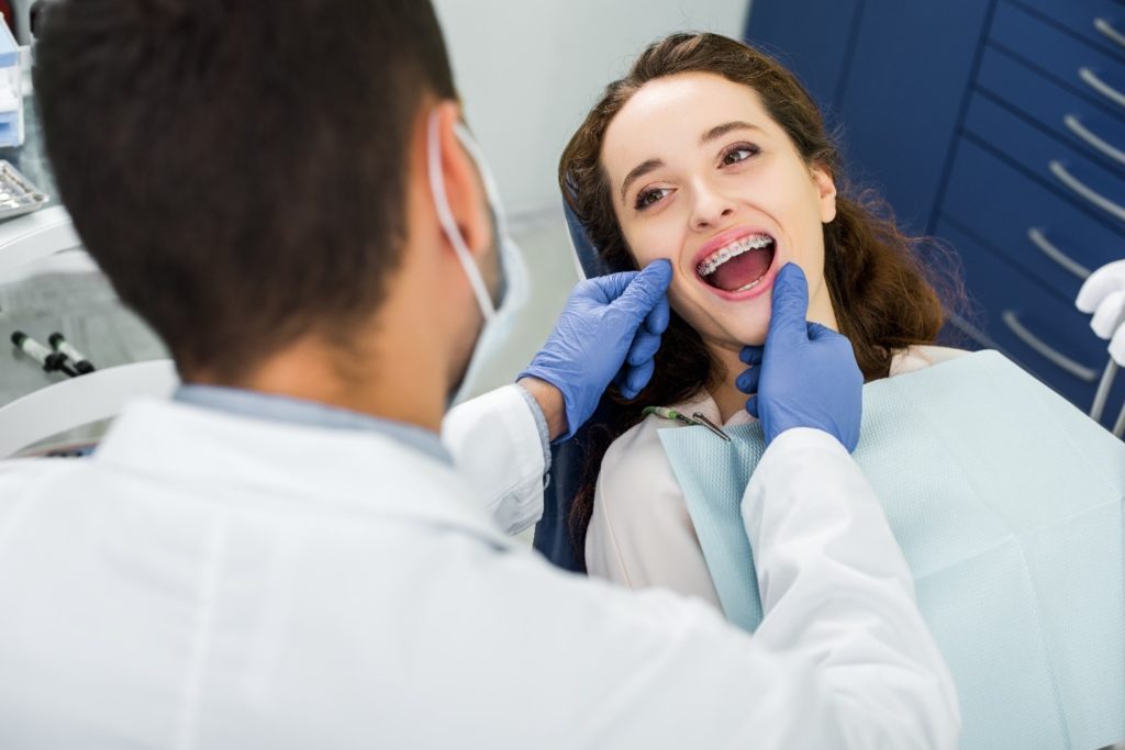 Orthodontist examining patient with traditional braces