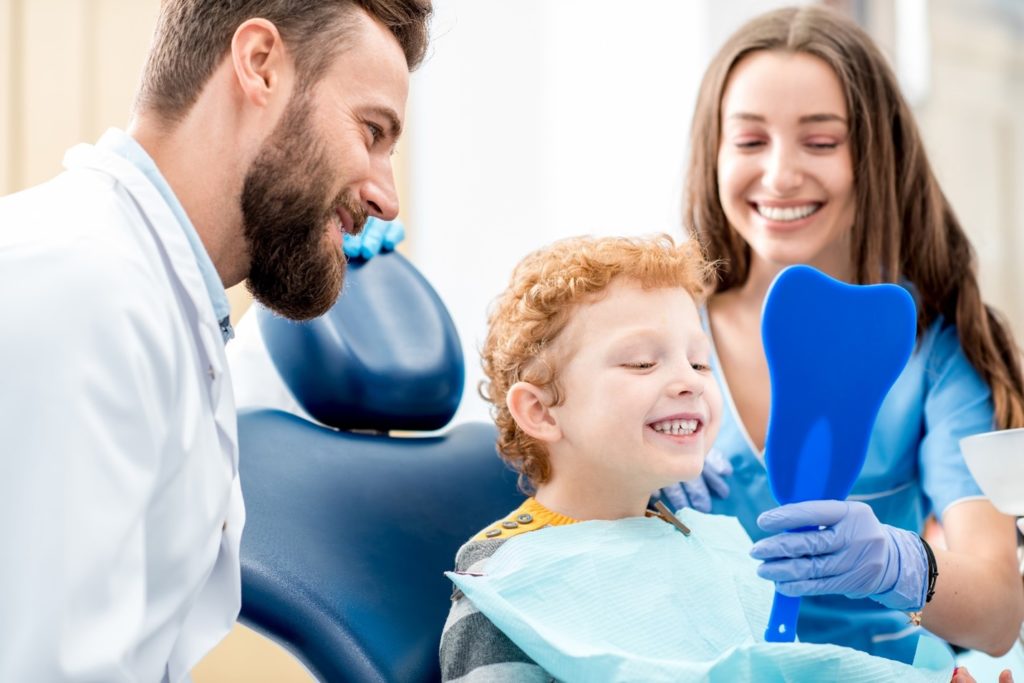 Kid smiling while looking in mirror at dentist’s appointment