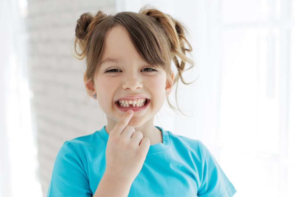 Child smiling while pointing to missing tooth