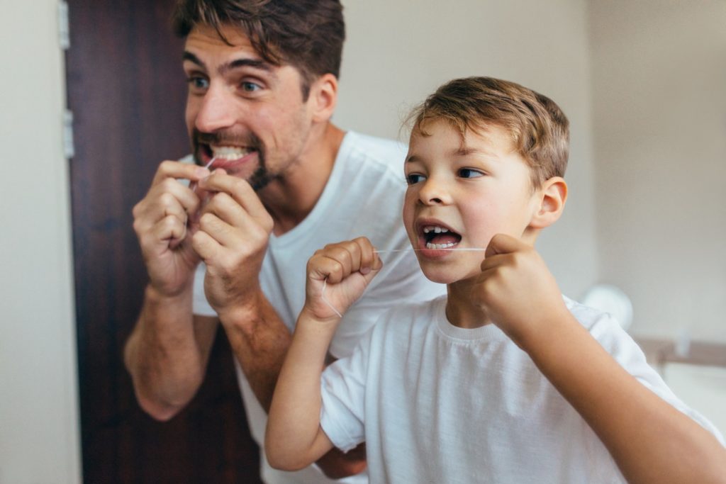 Father and son smiling while flossing their teeth in bathroom
